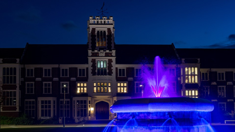 a night time view of the fountain flood lit in purple and the Hazlerigg building in the background